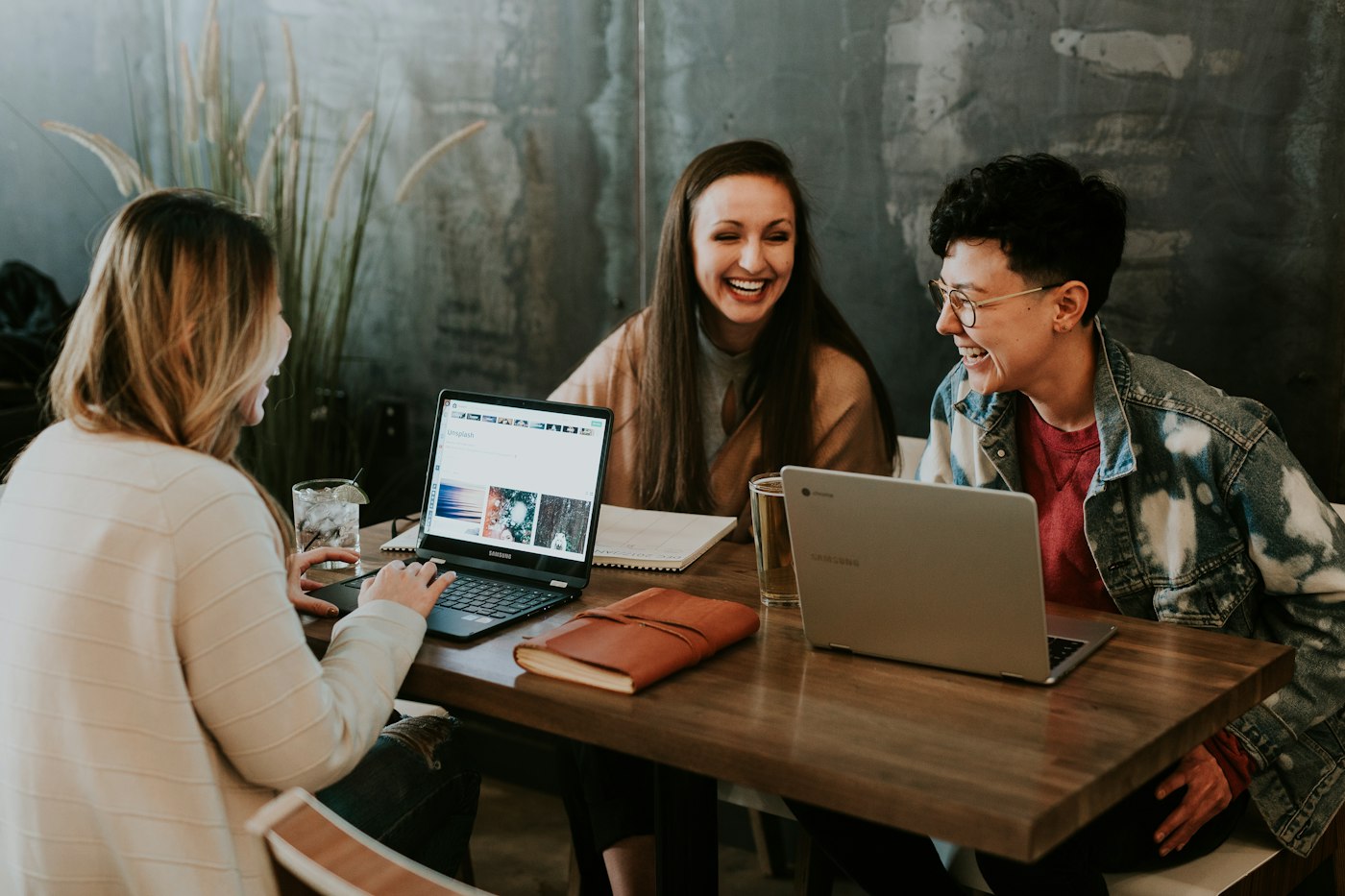 Three students laughing while planning together at a table with a laptop